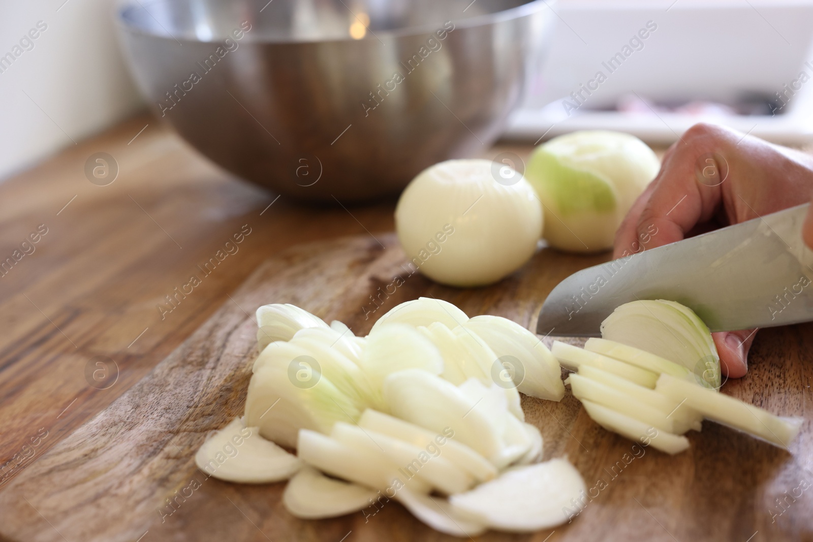 Photo of Woman cutting fresh ripe onion on wooden board, closeup. Space for text