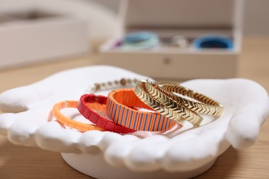 Photo of Ceramic hand stand with many different bracelets on wooden table, closeup