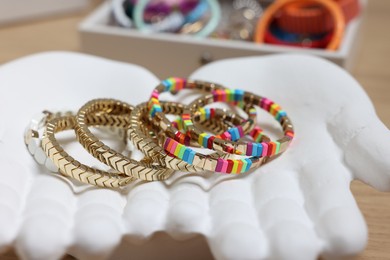 Photo of Ceramic hand stand with many different bracelets on table, closeup