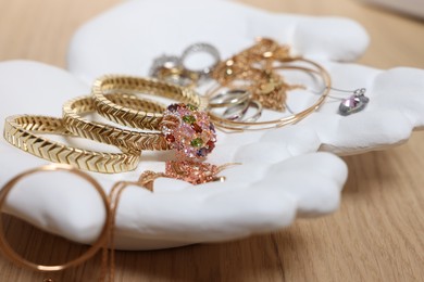 Photo of Ceramic hand stand with stylish bracelets and other accessories on wooden table, closeup