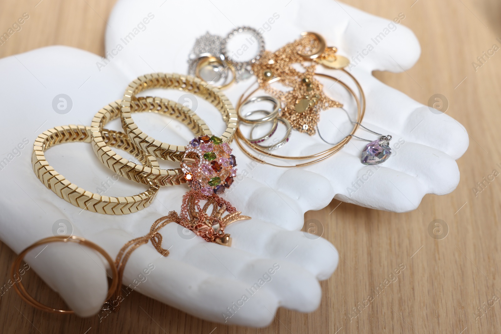 Photo of Ceramic hand stand with stylish bracelets and other accessories on wooden table, closeup