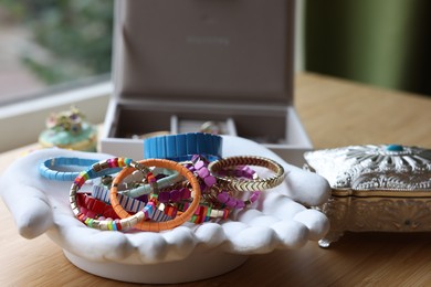 Ceramic hand stand with many stylish bracelets and jewelry boxes on wooden table, closeup