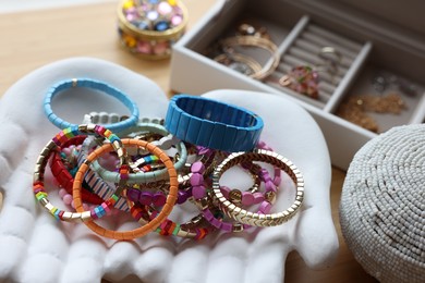 Photo of Ceramic hand stand with many stylish bracelets and jewelry boxes on wooden table, closeup