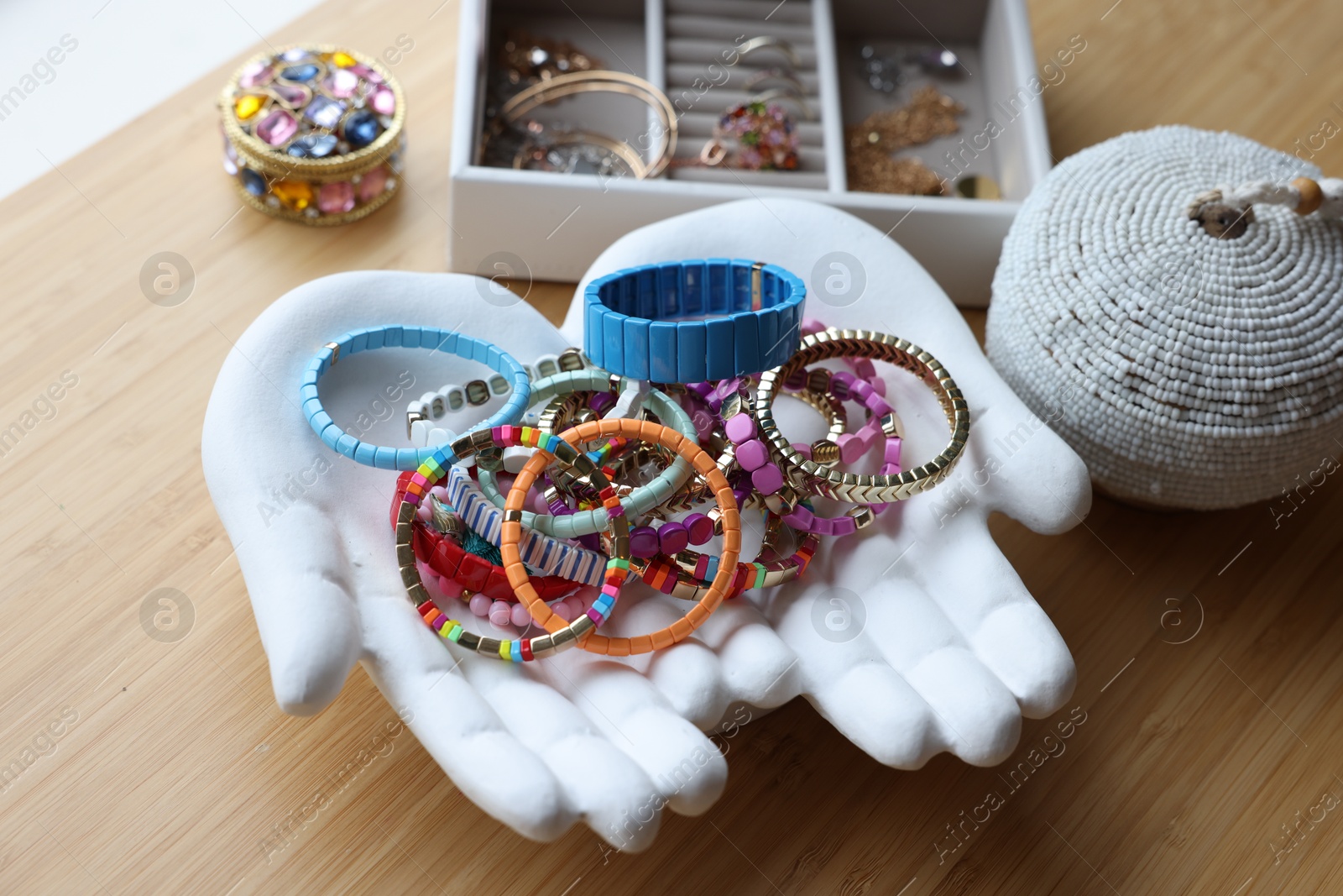 Photo of Ceramic hand stand with many stylish bracelets and jewelry boxes on wooden table