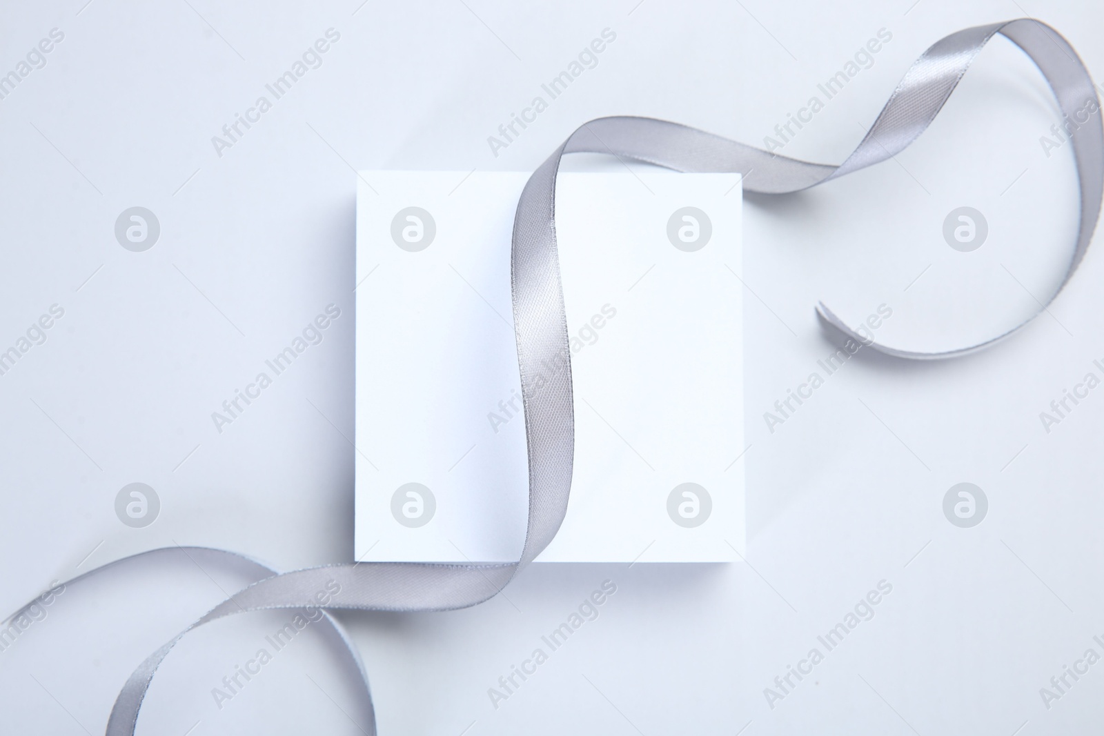 Photo of Beautiful grey ribbon and gift box on white background, top view