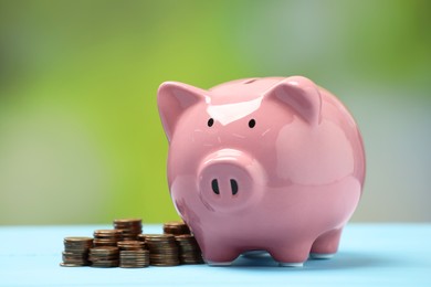 Pink piggy bank and stacks of coins on light blue table against blurred background