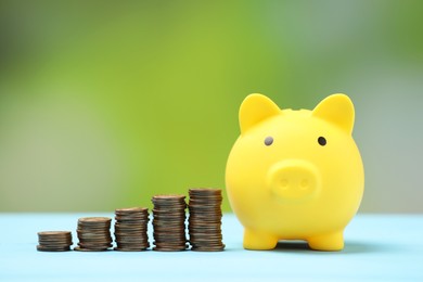 Yellow piggy bank and stacks of coins on light blue table against blurred background