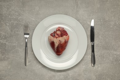 Photo of Raw heart, fork and knife on grey table, top view