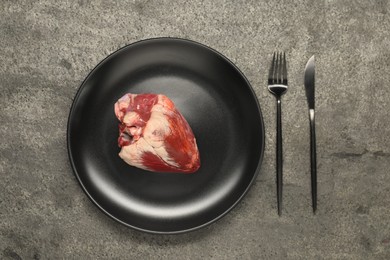 Photo of Raw heart, fork and knife on grey table, top view