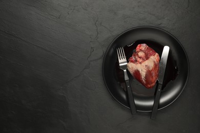 Raw heart, fork and knife on black table, top view. Space for text