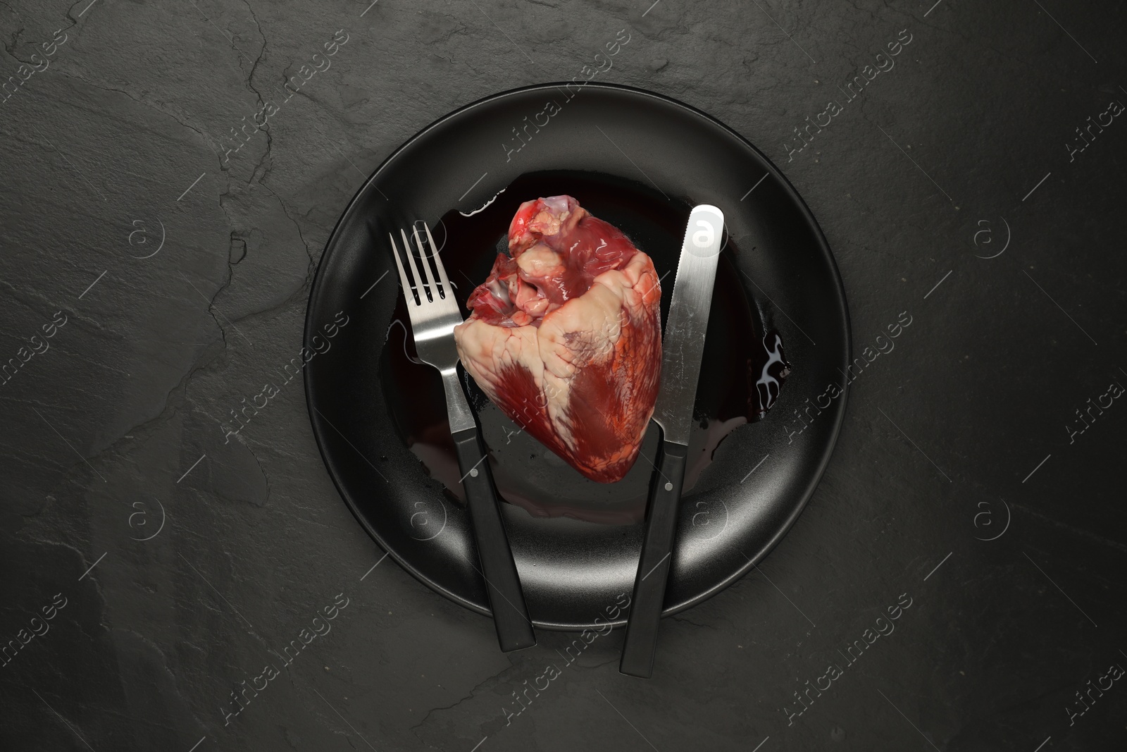 Photo of Raw heart, fork and knife on black table, top view