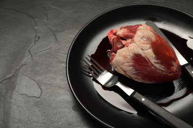 Photo of Raw heart, fork and knife on black table, space for text