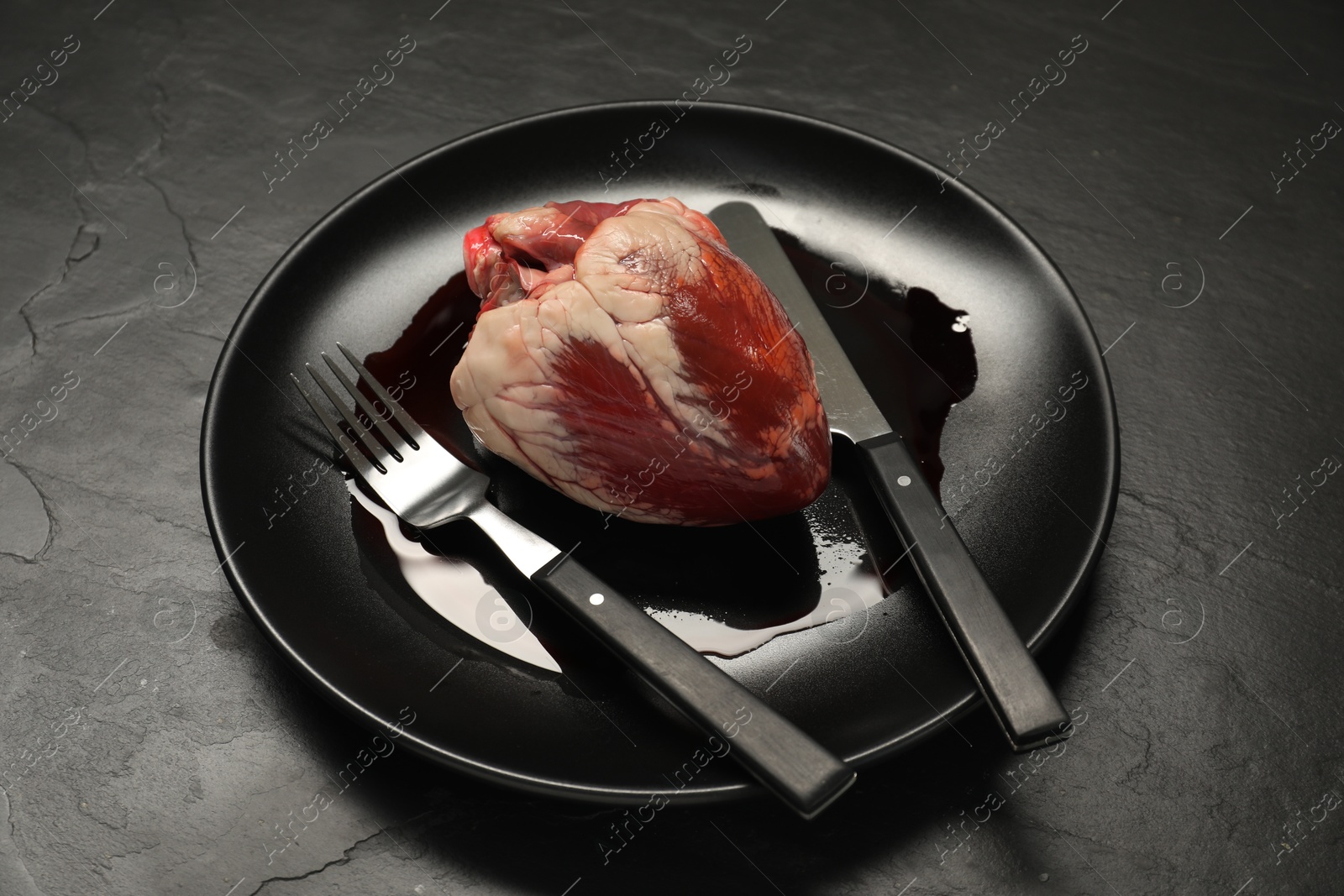 Photo of Raw heart, fork and knife on black table