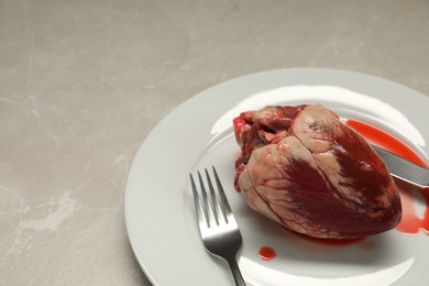 Raw heart, fork and knife on light grey marble table. Space for text