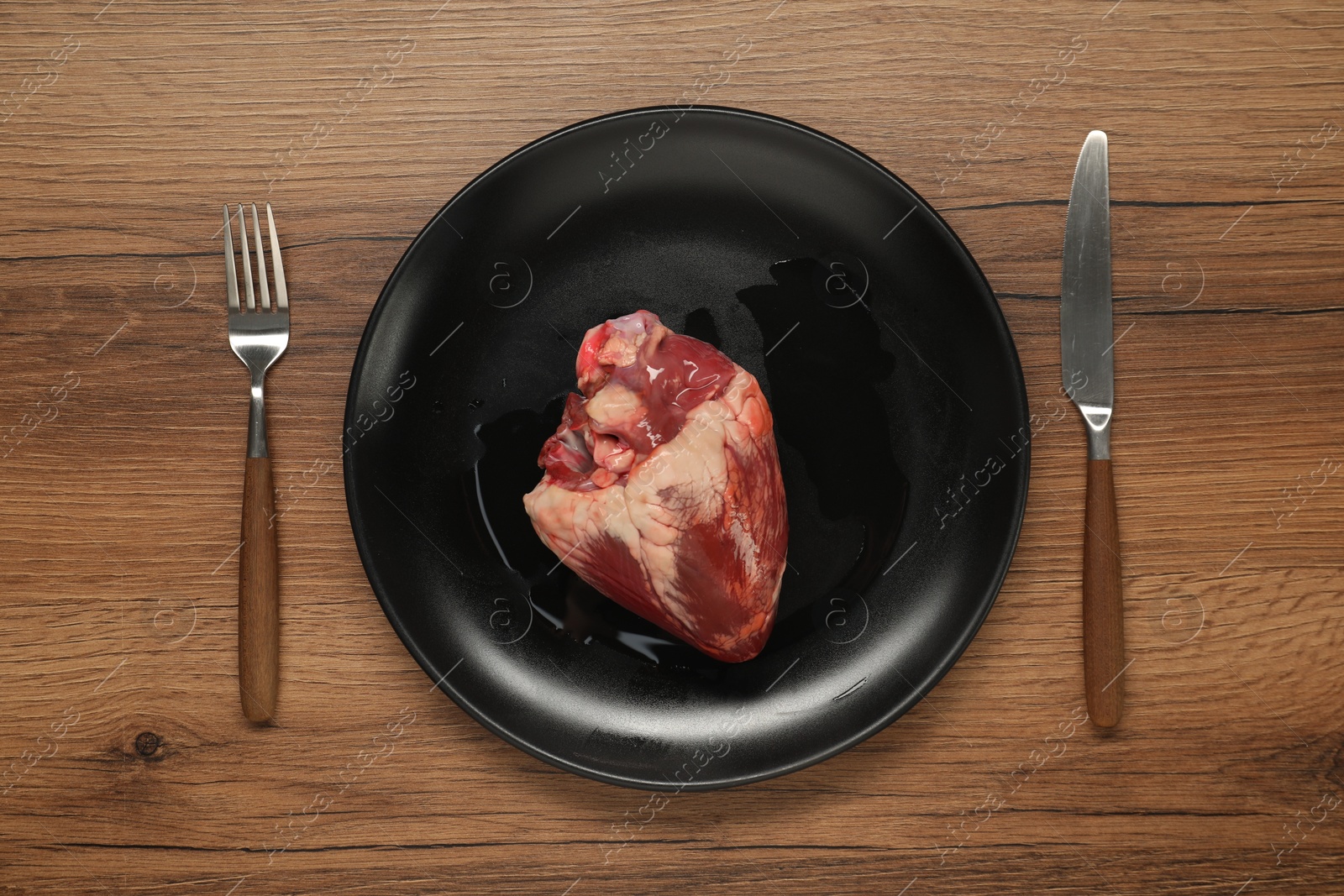 Photo of Raw heart, fork and knife on wooden table, top view