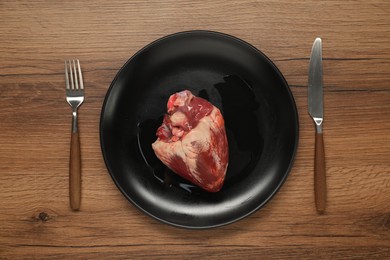 Raw heart, fork and knife on wooden table, top view