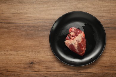 Photo of Raw heart on wooden table, top view. Space for text