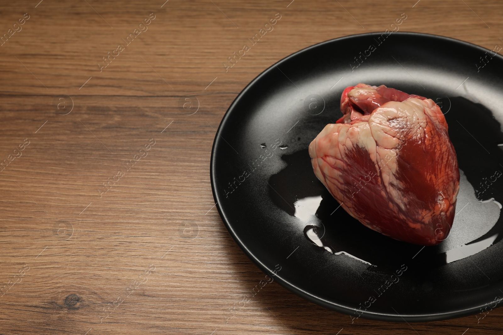 Photo of Raw heart on wooden table, space for text