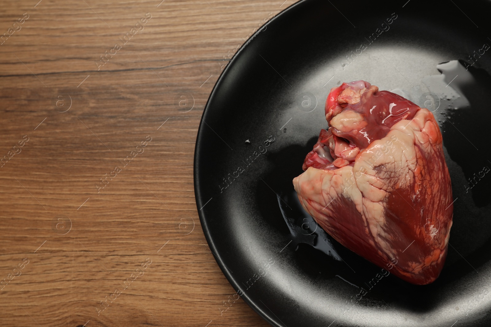 Photo of Raw heart on wooden table, top view. Space for text