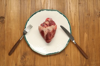 Raw heart, fork and knife on wooden table, top view