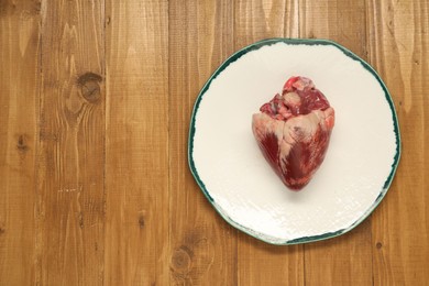 Photo of Raw heart on wooden table, top view. Space for text