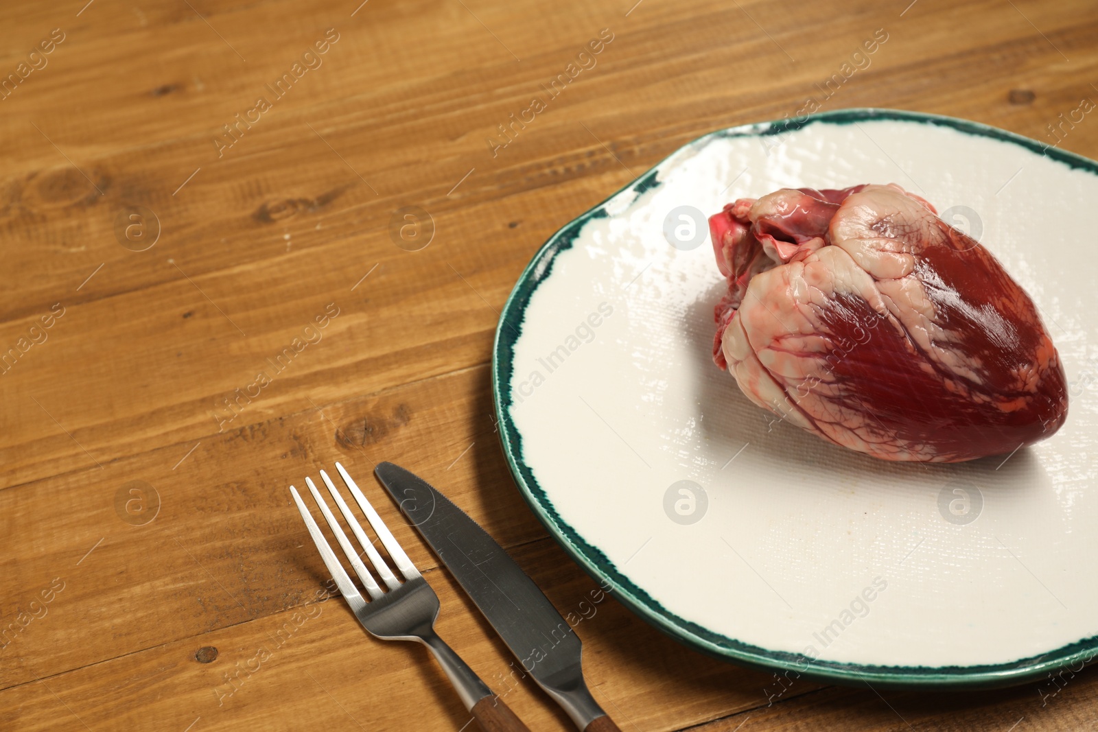 Photo of Raw heart, fork and knife on wooden table. Space for text