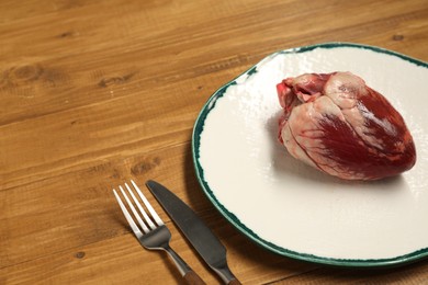 Raw heart, fork and knife on wooden table. Space for text