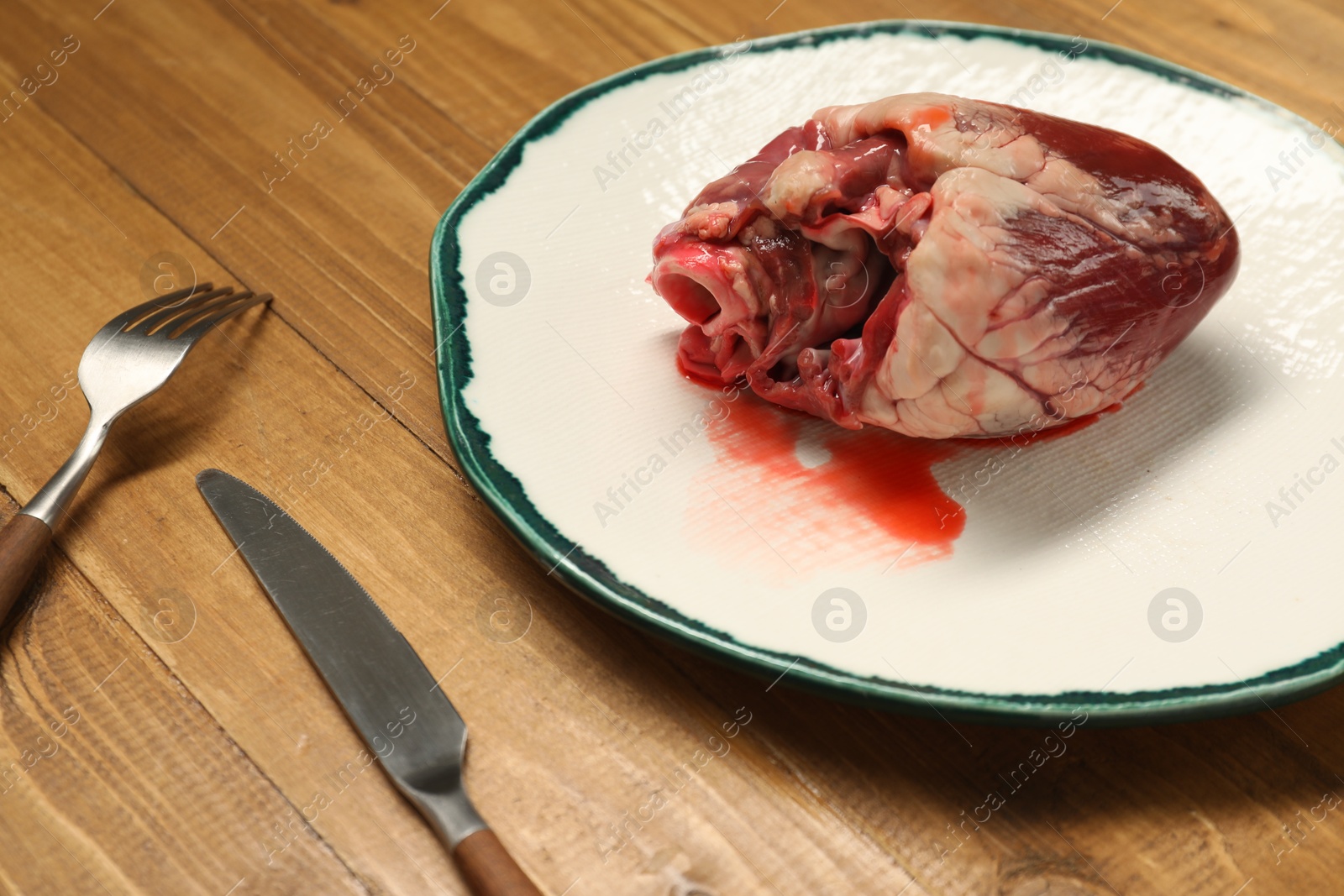 Photo of Raw heart, fork and knife on wooden table