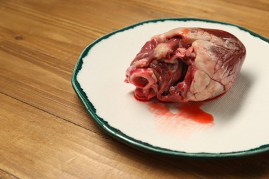 Raw heart and plate on wooden table. Space for text