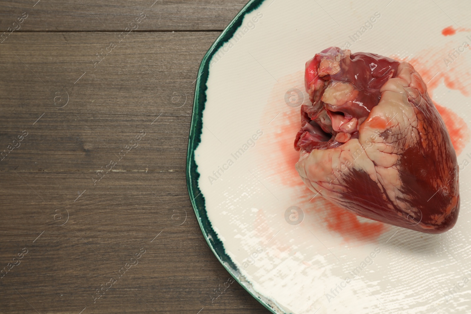 Photo of Raw pork heart on wooden table, top view. Space for text