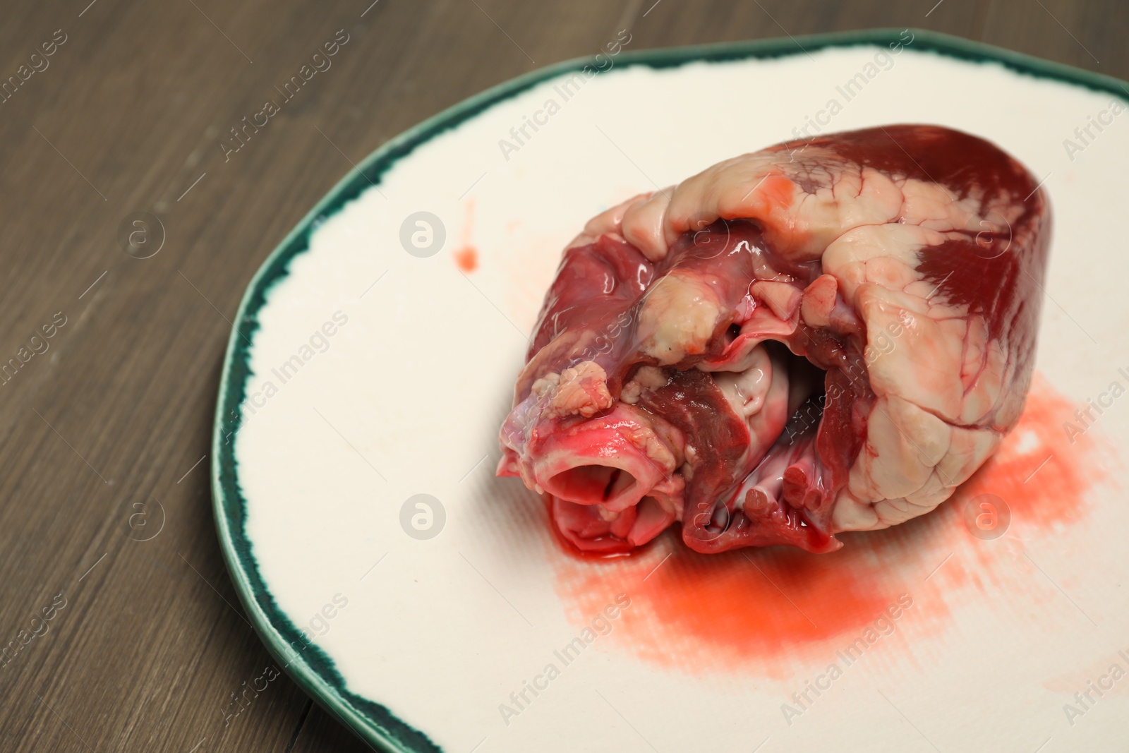 Photo of One raw pork heart on wooden table