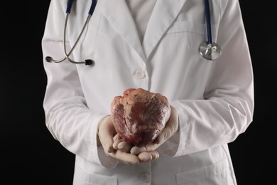 Photo of Doctor with heart on black background, closeup