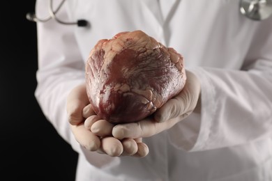 Photo of Doctor with heart on black background, closeup