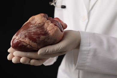 Photo of Doctor with heart on black background, closeup