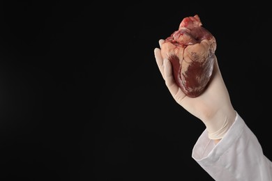 Photo of Doctor with heart on black background, closeup. Space for text