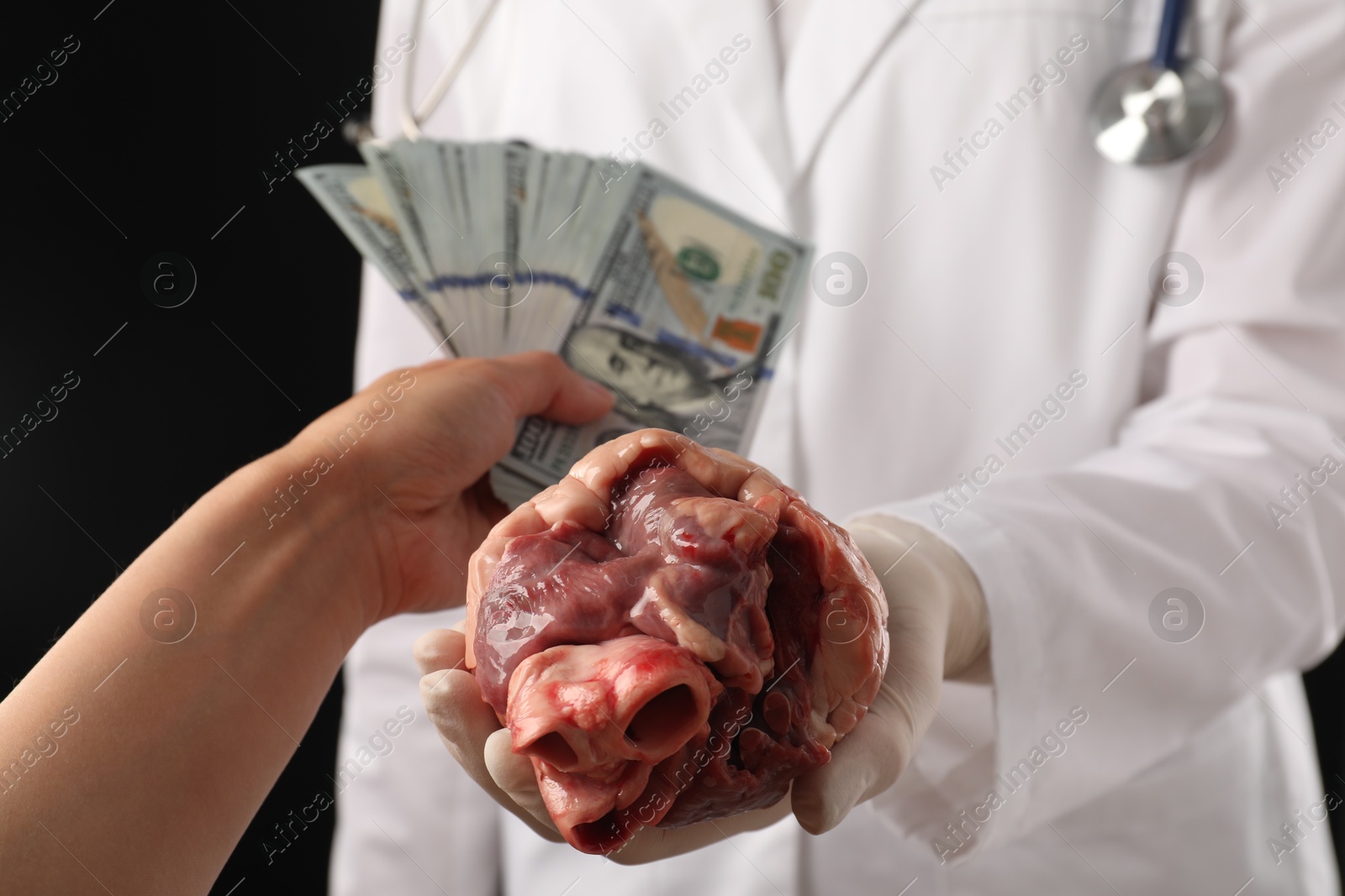 Photo of Patient giving dollar banknotes to doctor with heart on black background, closeup