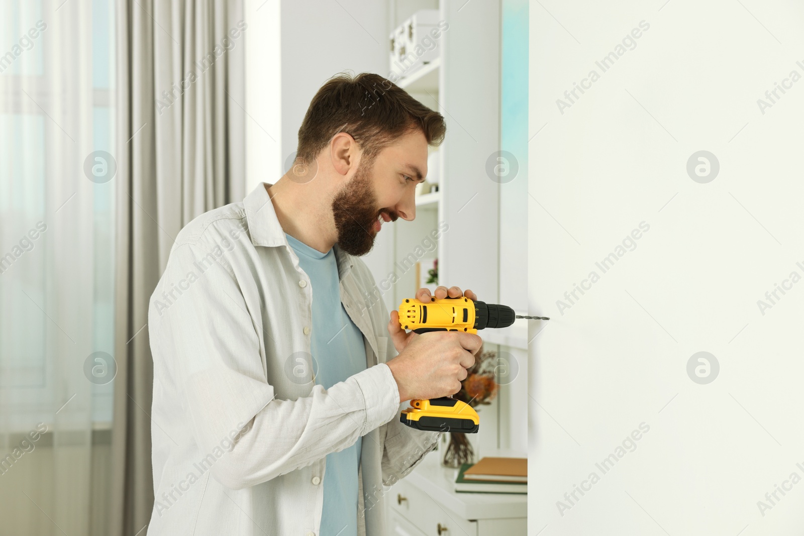 Photo of Smiling man drilling white wall at home