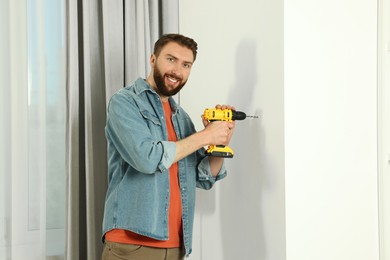 Smiling man drilling white wall at home