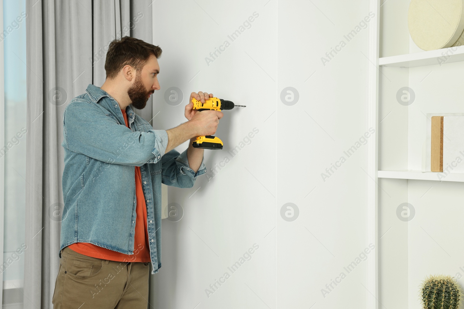 Photo of Man drilling wall at home. Space for text