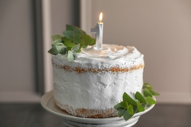 Photo of Tasty Birthday cake with burning candle and eucalyptus branches on grey table, closeup