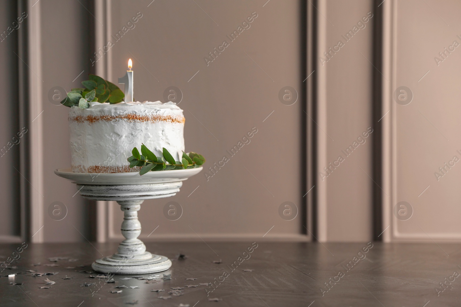 Photo of Tasty Birthday cake with burning candle and eucalyptus branches on grey table, space for text