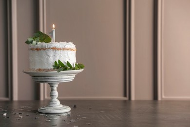 Photo of Tasty Birthday cake with burning candle and eucalyptus branches on grey table, space for text