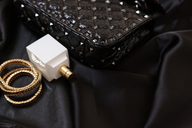 Leather bag, bottle of perfume and golden bracelets on black fabric, closeup. Space for text