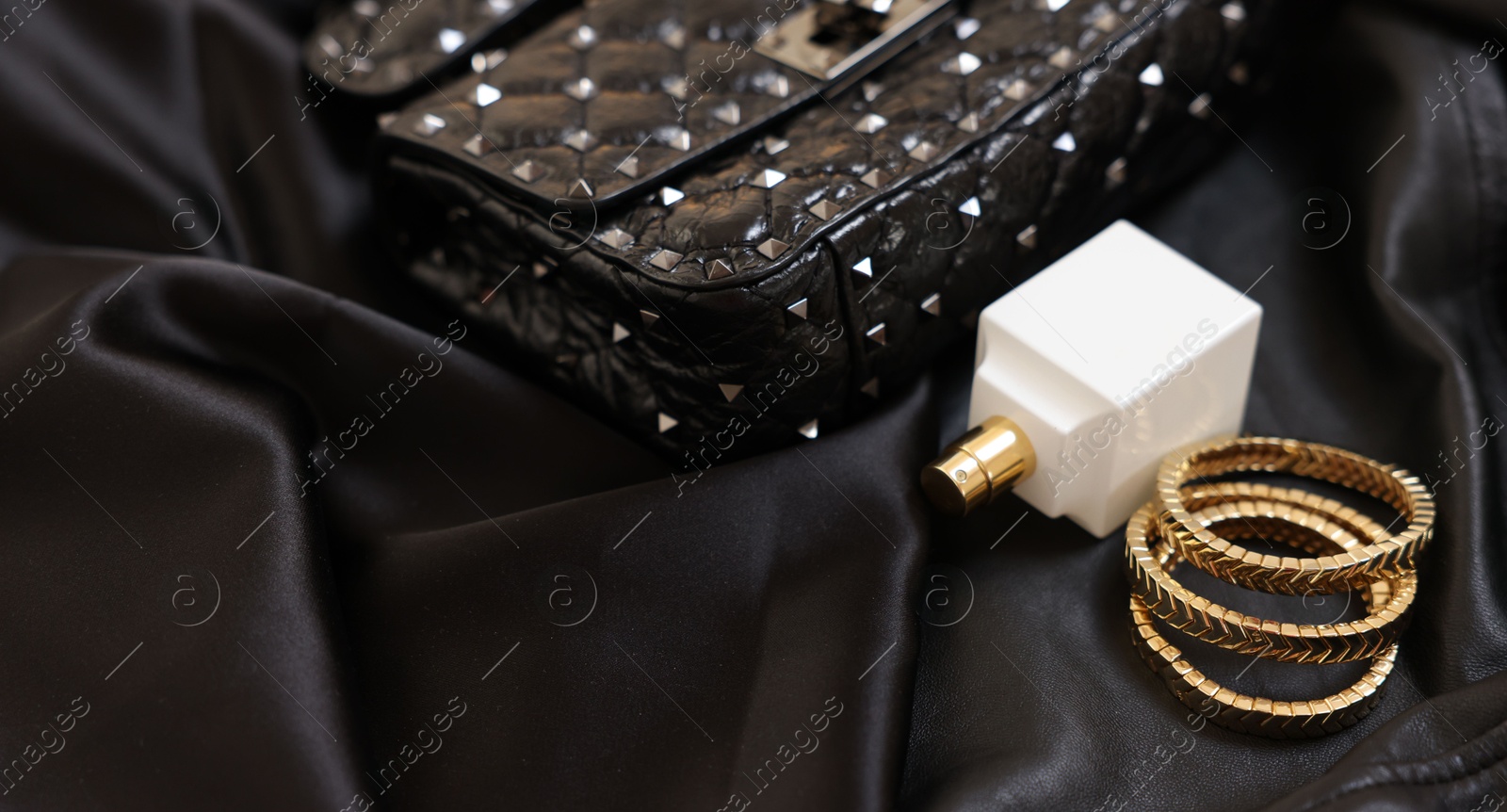 Photo of Leather bag, bottle of perfume and golden bracelets on black fabric, closeup. Space for text