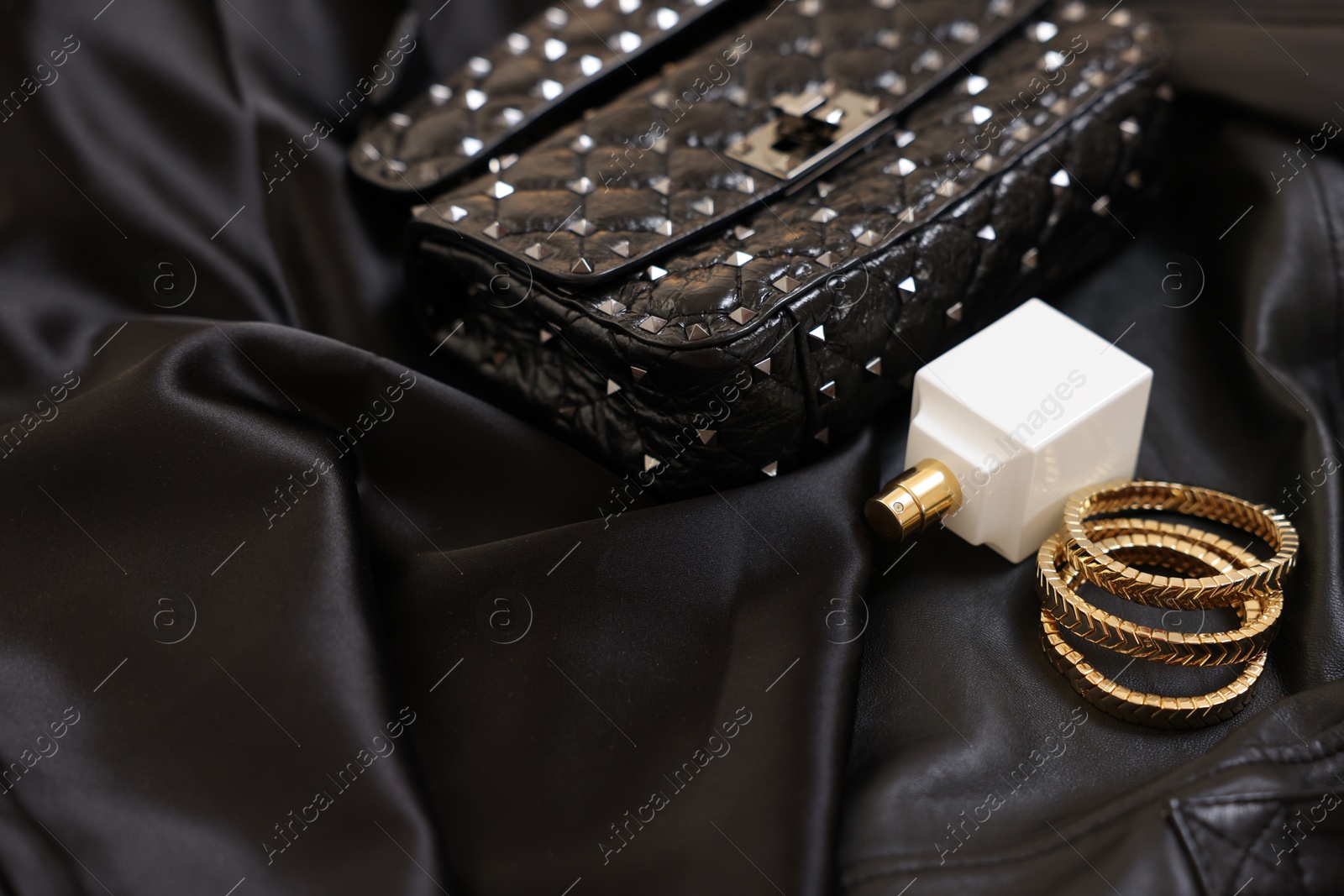 Photo of Leather bag, bottle of perfume and golden bracelets on black fabric, closeup. Space for text