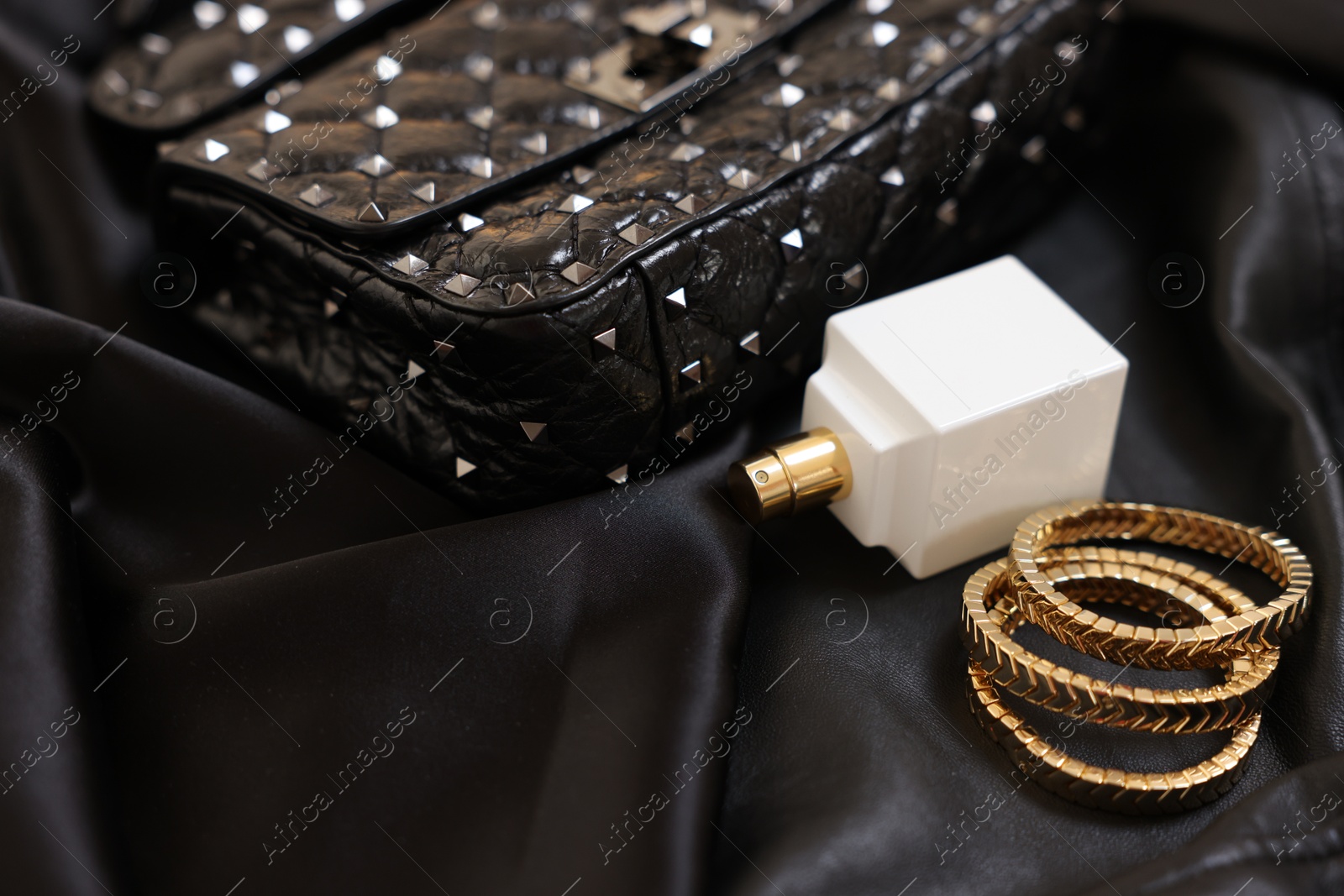 Photo of Leather bag, bottle of perfume and golden bracelets on black fabric, closeup. Space for text