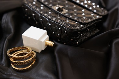 Photo of Leather bag, bottle of perfume and golden bracelets on black fabric, closeup. Space for text