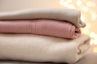 Photo of Stack of folded clothes on grey table against blurred lights, closeup