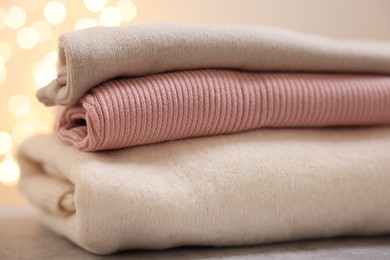 Photo of Stack of folded clothes on grey table against blurred lights, closeup