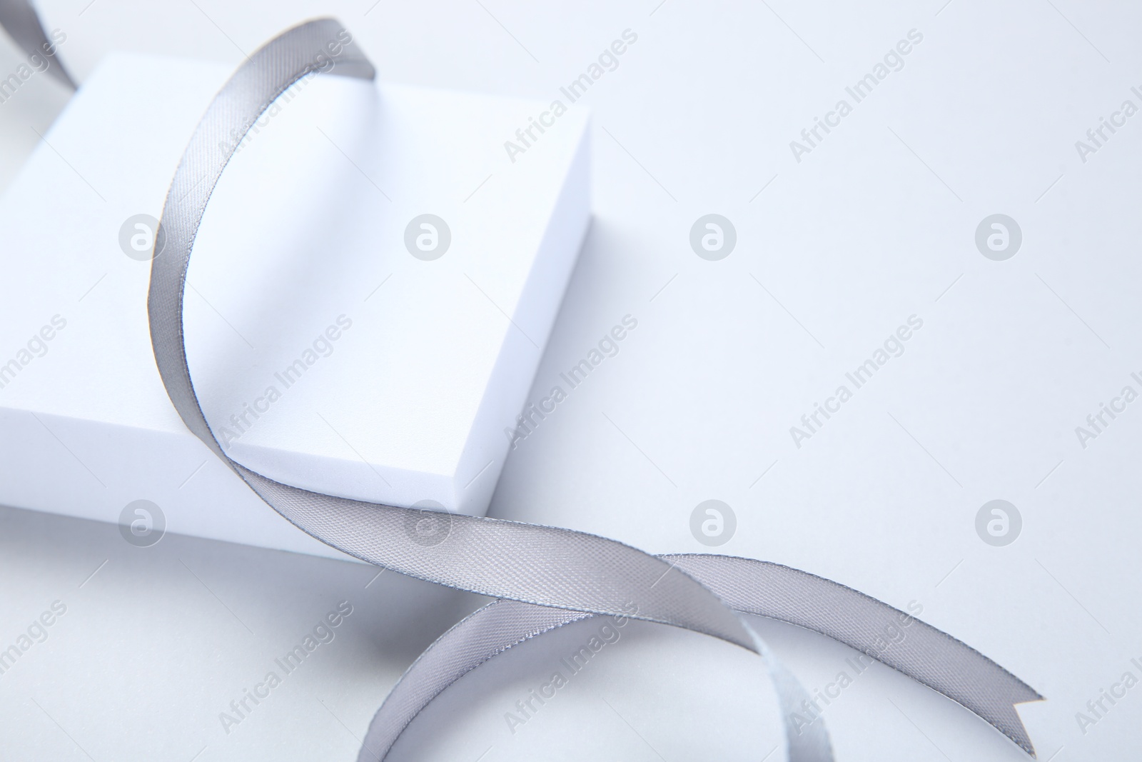 Photo of Beautiful grey ribbon and gift box on white background, space for text